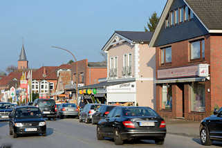 4097 Einzelhuser, Geschfte - dichter Strassenverkehr auf der Kieler Strasse in Quickborn; im Hintergrund der Kirchturm der Marienkirche.