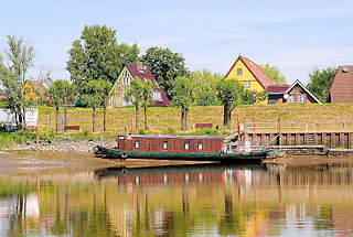 8756 Blick von der Str auf Wewelsfleet - ein Hausboot liegt bei Niedrigwasser im Schlick - hinter dem Deich Huser des Dorfes.